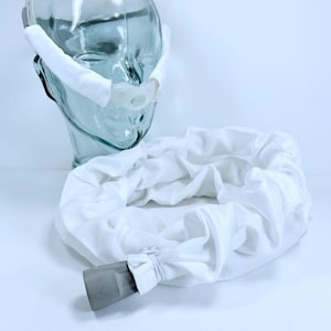 May include: A white CPAP mask and tubing set. The mask features a nose piece and headgear, with a white fabric tube connected to a gray connector. The set is displayed on a glass head form.