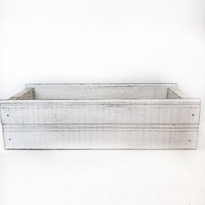 May include: White wooden box with a distressed finish. The box has a rectangular shape and is made of wood planks.