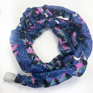 May include: A blue neck gaiter with a repeating pattern of a starry night sky, trees, and mountains in pink, green, and black. The gaiter has a gray plastic piece attached to one end.