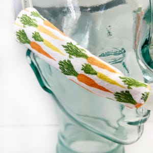 May include: A white fabric tube with a carrot print. The tube is wrapped around a clear glass object.