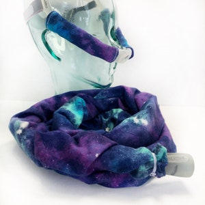May include: A CPAP machine with a clear mask and a galaxy-print fabric cover in shades of blue, purple, and white. The cover is wrapped around the hose and the mask straps are covered with matching fabric.