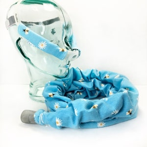 May include: A blue fabric tube with a daisy and bee pattern. The tube is designed to cover a CPAP hose. The tube is shown on a clear plastic head model with a CPAP mask attached.