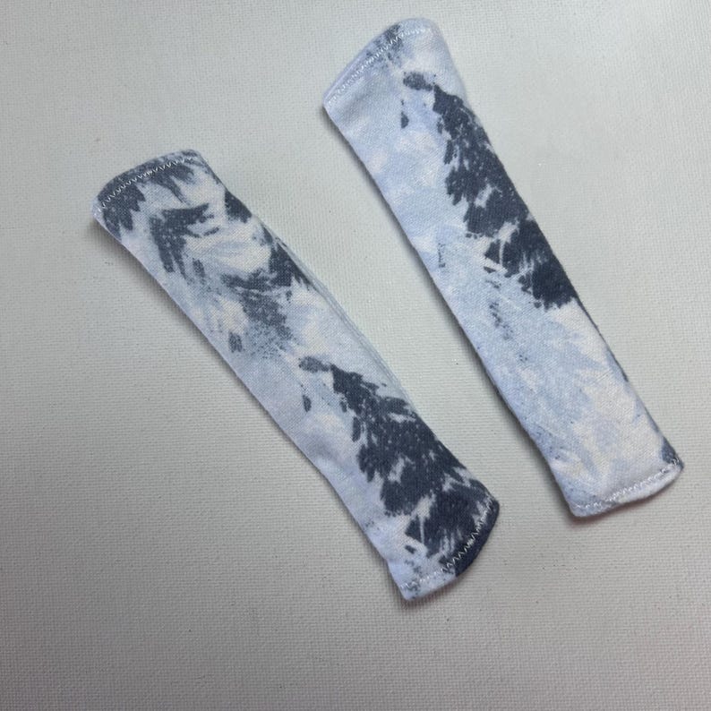 Pu&ograve; includere: Due coperture in tessuto rettangolari con un motivo tie-dye in tonalit&agrave; grigio antracite scuro e azzurro. Ogni pezzo ha estremit&agrave; arrotondate e un bordo cucito visibile, con un aspetto morbido e strutturato.