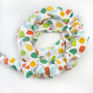 May include: White fabric scrunchie with a repeating pattern of colorful Easter eggs and yellow chicks.