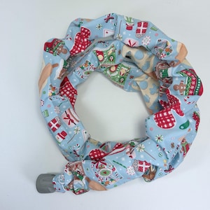 May include: A circular, fabric-covered item with a light blue background and a repeating Christmas-themed pattern. The pattern includes gingerbread men, wrapped gifts, snowflakes, and red and white checkered elements. The item has a gray, cylindrical end.