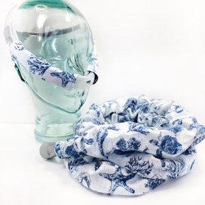 May include: A white fabric headband with a blue and white seashell print. The headband is designed to hold a CPAP mask in place. The headband is shown on a glass mannequin head.
