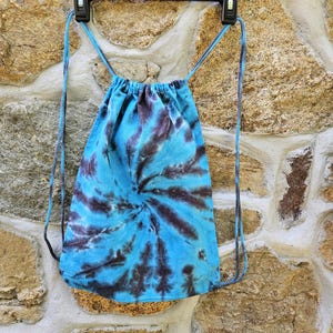 May include: A blue and black tie-dye drawstring bag hanging on a hanger. The bag is made of a soft, cotton fabric and has a simple design.