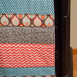 Könnte beinhalten: Eine bunte Patchwork-Decke mit verschiedenen Mustern, darunter Punkte, Zickzack und Paisley. Die Decke liegt über einem schwarzen Nachttisch.