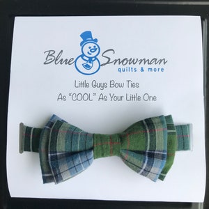 Puede incluir: Una pajarita de cuadros verdes y azules con una raya roja. La pajarita está sobre una tarjeta blanca con el texto "Blue Snowman quilts & more" y "Little Guys Bow Ties As "COOL" As Your Little One".