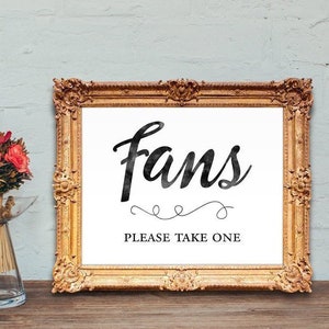 May include: A gold framed sign with the word "fans" in black script lettering. The sign also says "Please take one" in black text.