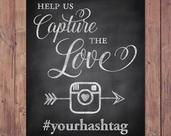 Puede incluir: Señal negra de pizarra con texto blanco que dice "Help us capture the love #yourhashtag". Un contorno blanco de una cámara de Instagram con un corazón dentro está por encima del hashtag. Una flecha blanca apunta hacia la izquierda y la derecha de la cámara.
