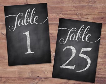 May include: Two black chalkboard table number signs with white chalk lettering. The first sign says "Table 1" and the second sign says "Table 25".
