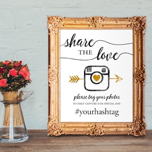 May include: A white sign in a gold frame with the text "share the love" in black script. A gold arrow points to a black and gold Instagram camera icon with a gold heart. The text "please tag your photos to help capture our special day: #yourhashtag" is below the icon.