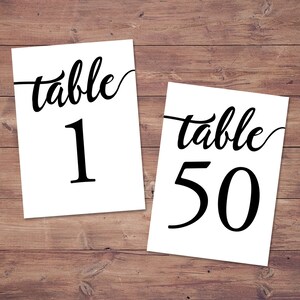 May include: Two white table number cards with black calligraphy. The first card says "table 1" and the second card says "table 50".