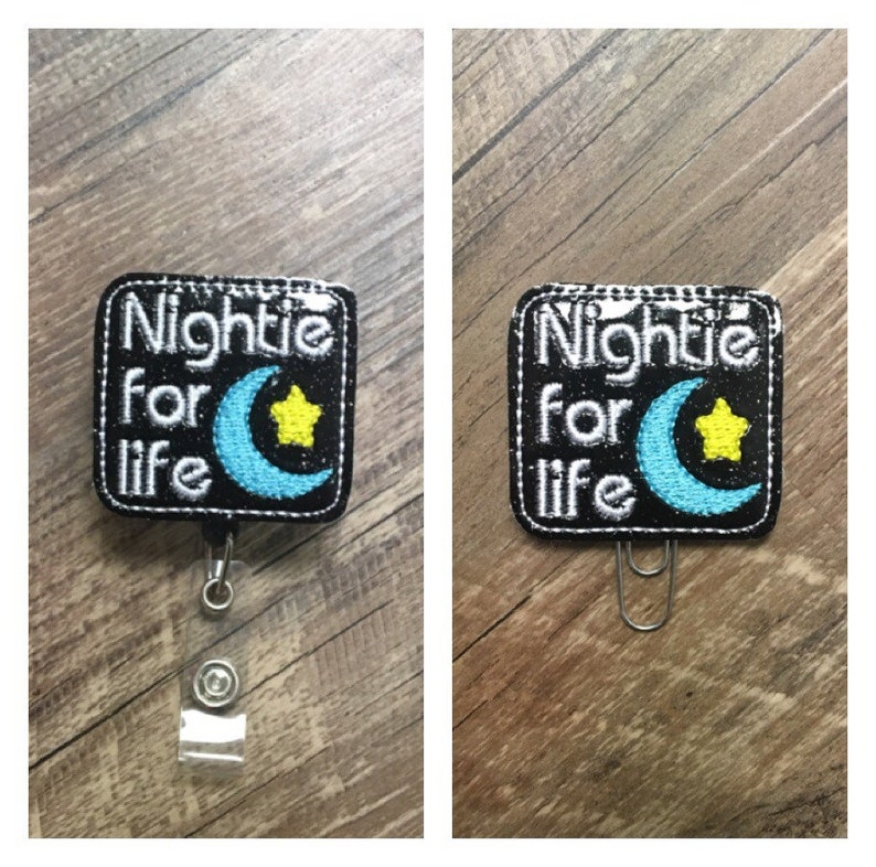 May include: Black badge reel with the text "Nightie for life". The badge features a blue crescent moon and a yellow star. The badge reel has a clear plastic strap and a metal clip.