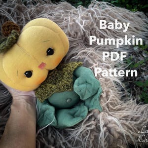 May include: A handmade plush pumpkin toy with a green crocheted hat and a green leaf stem. The toy is sitting on a fluffy brown surface. The text "Baby Pumpkin PDF Pattern" is visible in the image.