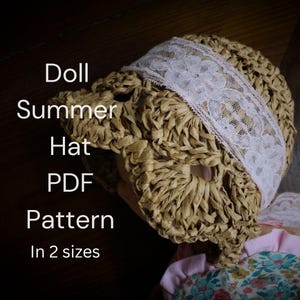 Op de afbeelding: Een zomerhoedje voor poppen gemaakt van geweven stro, met een witte kanten band. De hoed heeft een ronde kroon en een rand. De tekst "Doll Summer Hat PDF Pattern In 2 sizes" is zichtbaar.