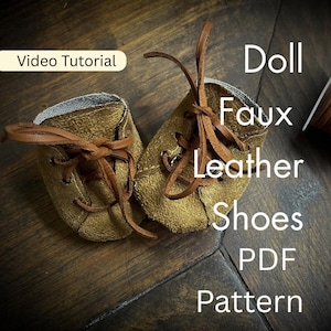 May include: A pair of olive-colored faux leather doll shoes with brown laces and a light-colored interior lining. The image includes the text "Video Tutorial" and "Doll Faux Leather Shoes PDF Pattern" overlaid on the shoes.