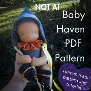 May include: A handmade fabric doll wearing a blue pointed hood, an orange ruffled collar, and dark blue polka-dot booties. The text reads: NOT AI Baby Haven PDF Pattern. Human made pattern and tutorial La Chulona.