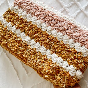 May include: A crocheted throw blanket with stripes of mustard yellow, white, and blush pink. The blanket is made with a soft, fuzzy yarn.