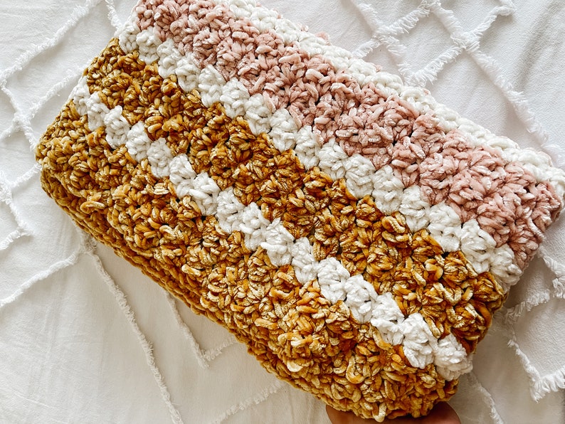 May include: A crocheted throw blanket with stripes of mustard yellow, white, and blush pink. The blanket is made with a soft, fuzzy yarn.