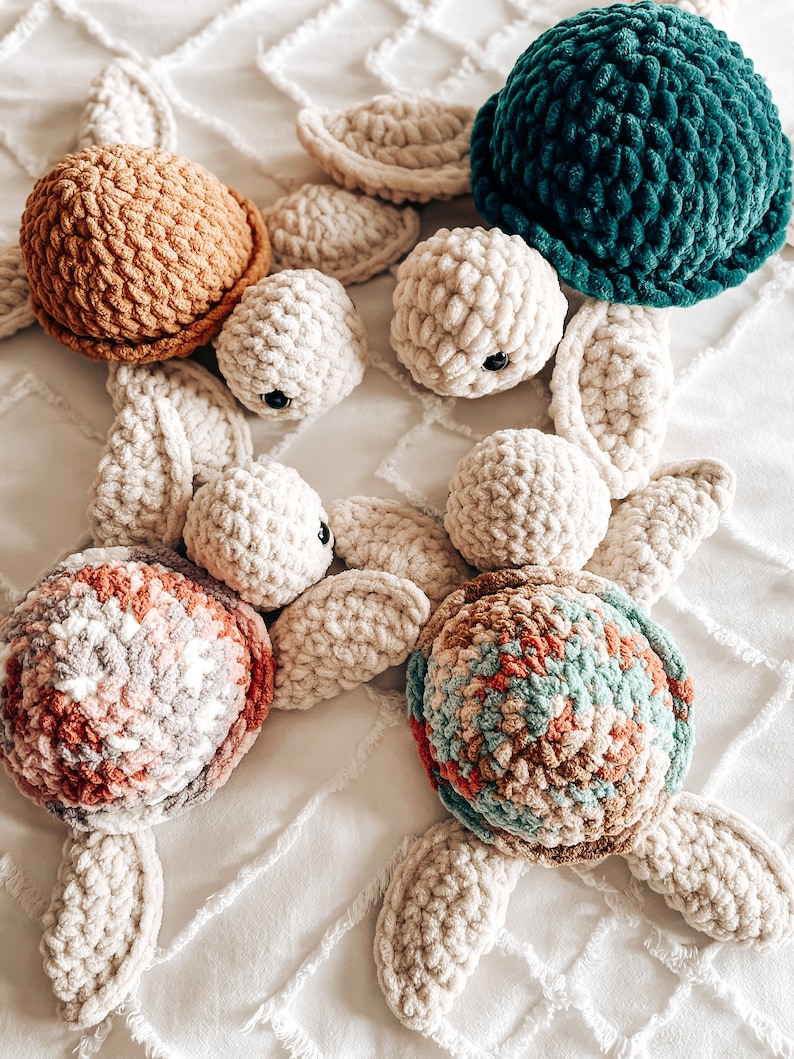 Puede incluir: Cinco juguetes de tortuga marina de crochet. Uno es de color verde azulado, otro es marr&oacute;n y tres son blancos con caparazones de diferentes colores. Las tortues blancas tienen caparazones rosas, azules y marrones.