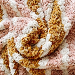 May include: A soft, cozy blanket with stripes of pink, white, and mustard yellow. The blanket is made of a plush, velvety yarn and is perfect for cuddling up on the couch.