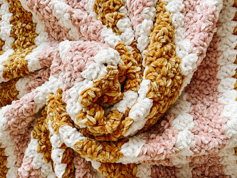 May include: A soft, cozy blanket with stripes of pink, white, and mustard yellow. The blanket is made of a plush, velvety yarn and is perfect for cuddling up on the couch.