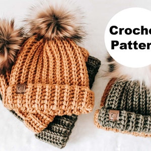May include: Two crocheted hats with faux fur pom poms. The larger hat is mustard yellow and the smaller hat is olive green. Both hats have a brown leather label with the letter "C" on them. Crochet Pattern.