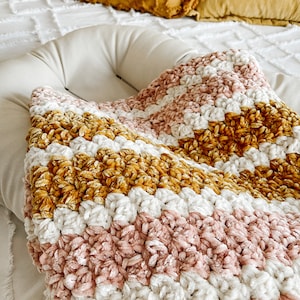 May include: A soft, plush blanket with stripes of pink, white, and mustard yellow. The blanket is made of a chenille yarn and has a fuzzy texture.
