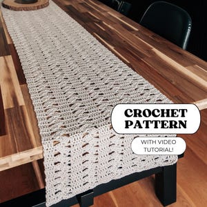 Puede incluir: Un camino de mesa de ganchillo en color beige claro con un patrón de puntos texturizados repetitivos. La imagen incluye el texto CROCHET PATTERN y WITH VIDEO TUTORIAL! El camino se muestra sobre una mesa de madera larga y pulida.