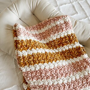 May include: A soft, striped crocheted blanket in shades of pink, white, and mustard yellow. The blanket is made with a fluffy yarn and has a textured, chunky look.