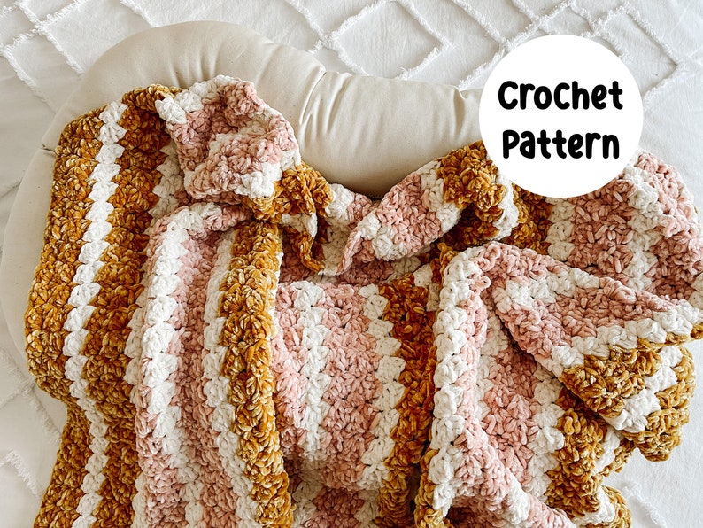 May include: A crocheted blanket with stripes of pink, white, and mustard yellow yarn. The blanket is made with a textured stitch and has a soft, fuzzy appearance. "Crochet Pattern" is written in white text on a white circle.