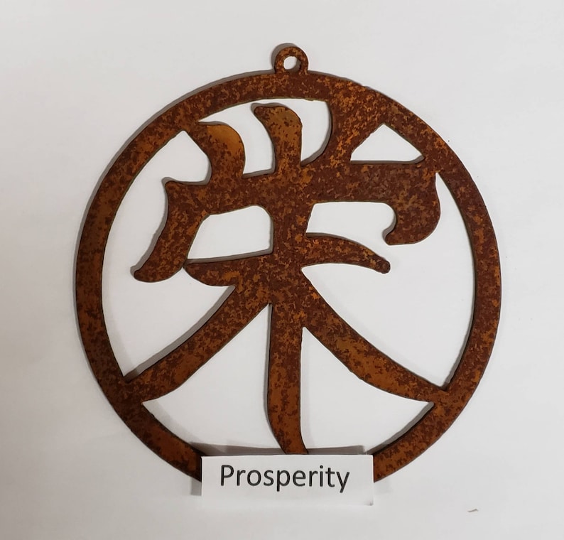 Może przedstawiać: Okrągły ornament z rdzawego metalu z wyciętym w środku chińskim znakiem oznaczającym "dobrobyt". Słowo "Prosperity" jest napisane pod okręgiem.