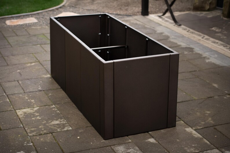 May include: A rectangular, dark brown metal planter box with a divided interior. The planter is empty and sits on a stone patio. The box is approximately 36 inches long, 18 inches wide, and 18 inches tall.