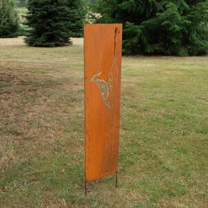 May include: A tall, rectangular, weathered metal garden art piece with a bird design. The artwork is a rusty orange color and stands on two metal legs, placed in a grassy outdoor setting.