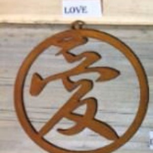 Może przedstawiać: Okrągły metalowy element w kolorze rdzy z wyciętym w środku chińskim znakiem oznaczającym "miłość". Słowo "LOVE" jest napisane na małej białej etykiecie nad okręgiem.
