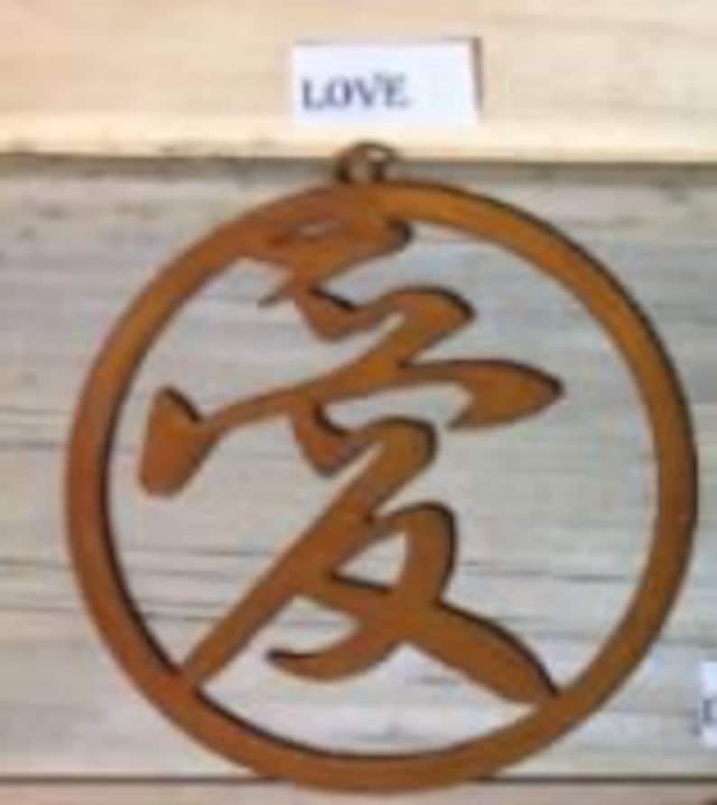 Może przedstawiać: Okrągły metalowy element w kolorze rdzy z wyciętym w środku chińskim znakiem oznaczającym "miłość". Słowo "LOVE" jest napisane na małej białej etykiecie nad okręgiem.