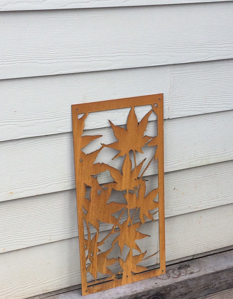 Op de afbeelding: Een roestig metalen wandkunstwerk met een uitgesneden ontwerp van bladeren. De bladeren zijn in een cluster gerangschikt en hebben een natuurlijke, organische uitstraling.