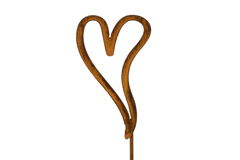 Puede incluir: Un estaca de jard&iacute;n de metal con forma de coraz&oacute;n y un acabado marr&oacute;n oxidado y desgastado. El contorno del coraz&oacute;n es asim&eacute;trico y abierto, con una fina varilla de metal que se extiende desde el centro inferior para sostener la pieza en el suelo.