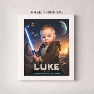 May include: Framed artwork featuring a baby holding a glowing blue lightsaber, set against a space-themed background with planets and spaceships. The name "LUKE" is displayed below the baby, with the text "THE FORCE IS STRONG WITH THIS ONE".