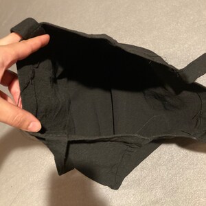May include: A black fabric bag with a rectangular opening and two straps. The bag is made of a soft, dark material. The interior of the bag is visible.