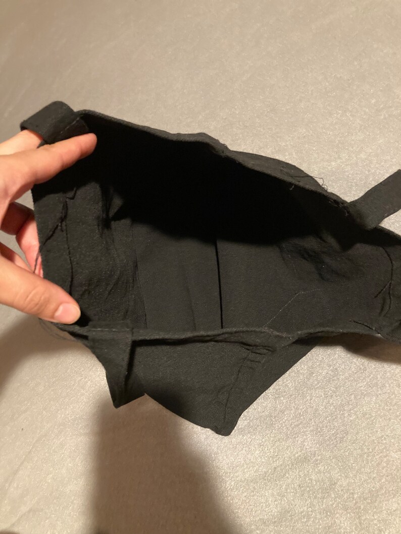 May include: A black fabric bag with a rectangular opening and two straps. The bag is made of a soft, dark material. The interior of the bag is visible.