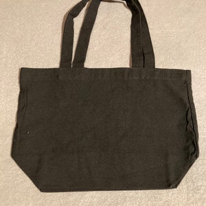 May include: A black tote bag with two handles. The bag is made of a sturdy fabric and has a rectangular shape. The handles are attached to the top of the bag and are long enough to be carried over the shoulder.