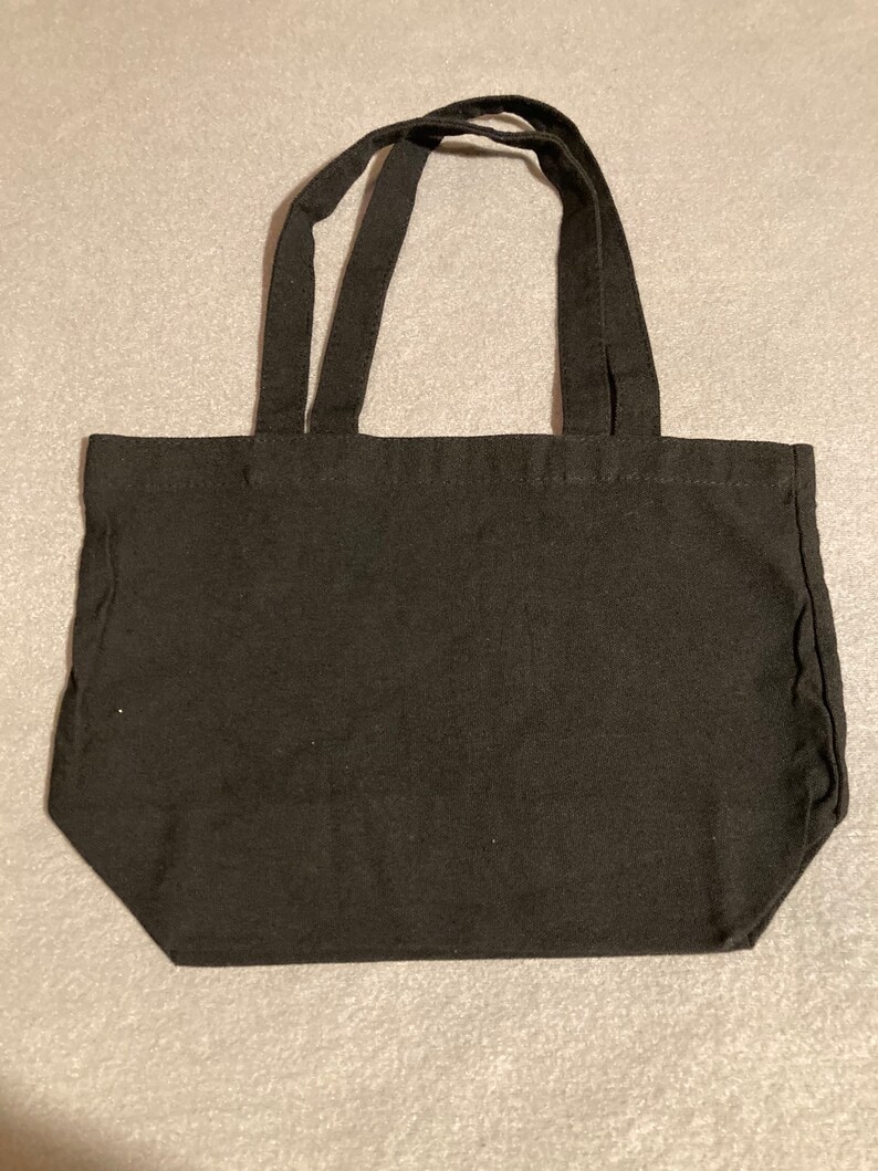 May include: A black tote bag with two handles. The bag is made of a sturdy fabric and has a rectangular shape. The handles are attached to the top of the bag and are long enough to be carried over the shoulder.
