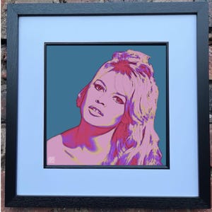 May include: Framed pop art print featuring a stylized portrait of a woman with pink and purple hair and skin tones against a teal background. The artwork is framed in a black wooden frame with a white mat.