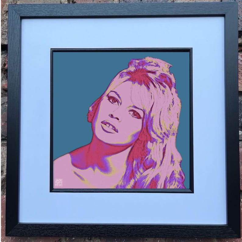 May include: Framed pop art print featuring a stylized portrait of a woman with pink and purple hair and skin tones against a teal background. The artwork is framed in a black wooden frame with a white mat.