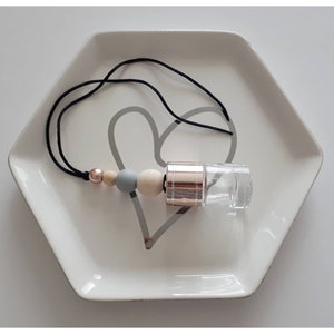 May include: A car air freshener with a clear glass bottle, a rose gold metal cap, and a black string. The string has wooden and grey beads.