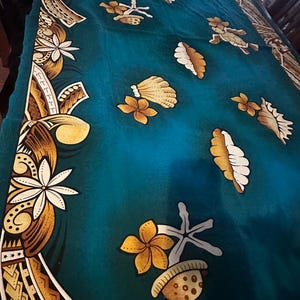 May include: Teal fabric with a detailed border featuring white flowers, geometric patterns, and brown accents. The fabric is adorned with stylized flowers, leaves, and seashell designs in shades of brown, white, and yellow.