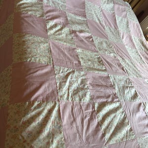 May include: A pink and white patchwork quilt with a floral pattern. The quilt is made of squares of different fabrics, some plain and some with a floral print.